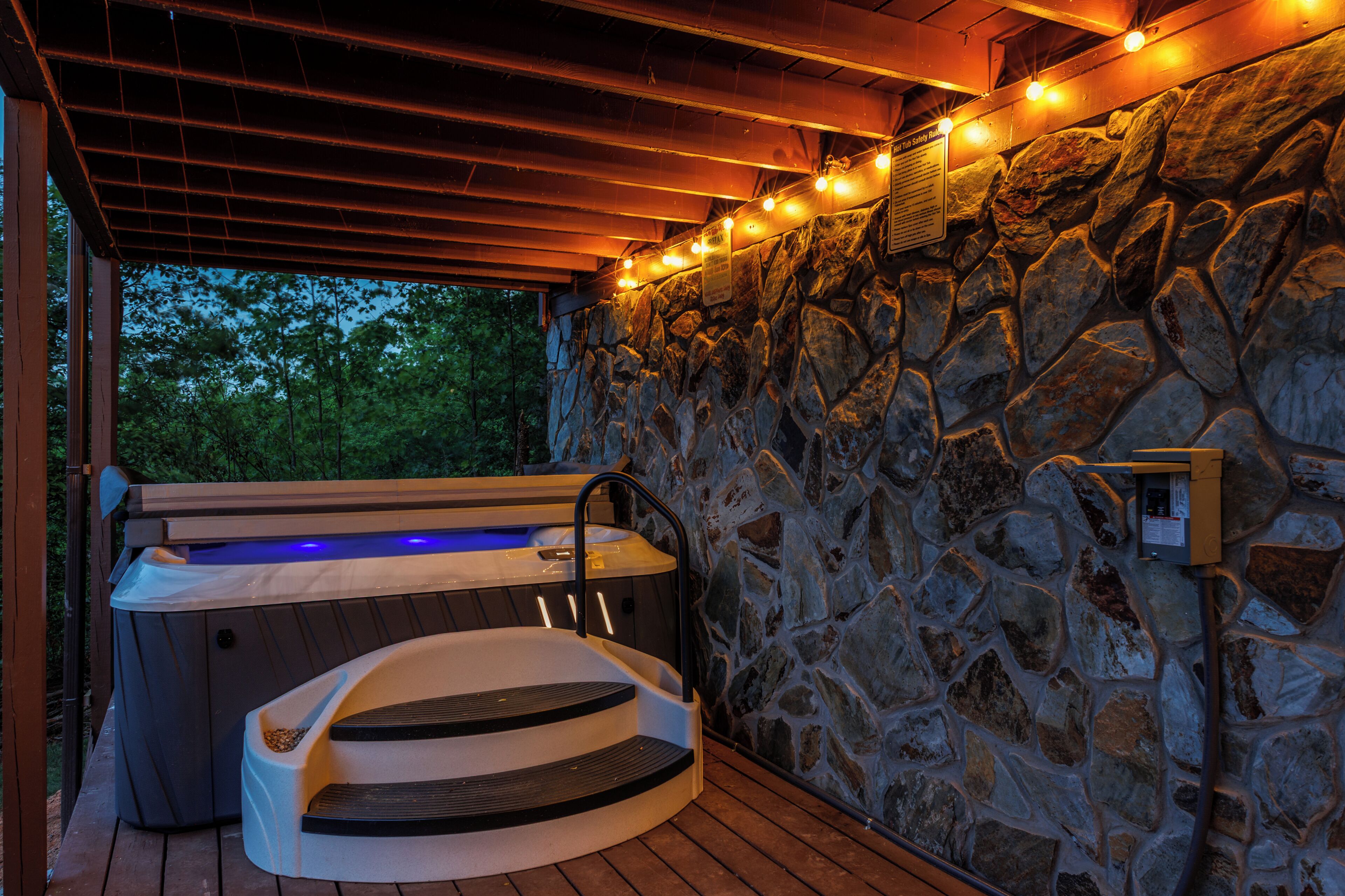 A hot tub with steps leading up to it, surrounded by a stone wall and wooden beams.