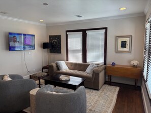 A living room with a sofa, armchairs, a coffee table, and a TV mounted on the wall. - 3 bedroom charming Heights cottage for relaxing under the trees (Houston)