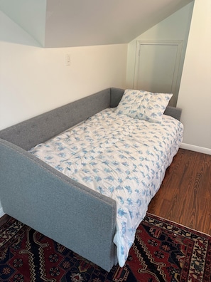 A single bed with a grey frame and a patterned duvet in a room with a wooden floor and a patterned rug. - 3 bedroom charming Heights cottage for relaxing under the trees (Houston)