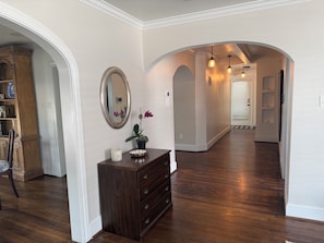 A hallway with wooden flooring, a dresser with drawers, a mirror, and a vase with flowers. - 3 bedroom charming Heights cottage for relaxing under the trees (Houston)