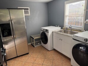 A compact kitchen with a stainless steel refrigerator, a washing machine, and a Samsung dishwasher. - 3 bedroom charming Heights cottage for relaxing under the trees (Houston)