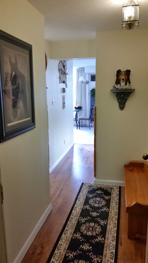 A hallway with a patterned rug, a framed picture on the wall, and a decorative wall piece.