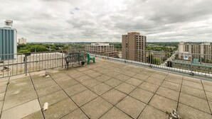 A rooftop terrace with a metal railing, a green chair, and a small table.