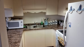 A kitchen with white cabinets, a microwave, a sink, and a refrigerator.