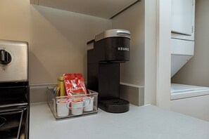 A kitchenette with a coffee maker, a refrigerator, and a clear plastic container holding coffee pods and a Tim Hortons bag.