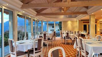 Un restaurante con varias mesas y sillas, amplios ventanales que ofrecen vistas al exterior y una estructura de techo de madera.