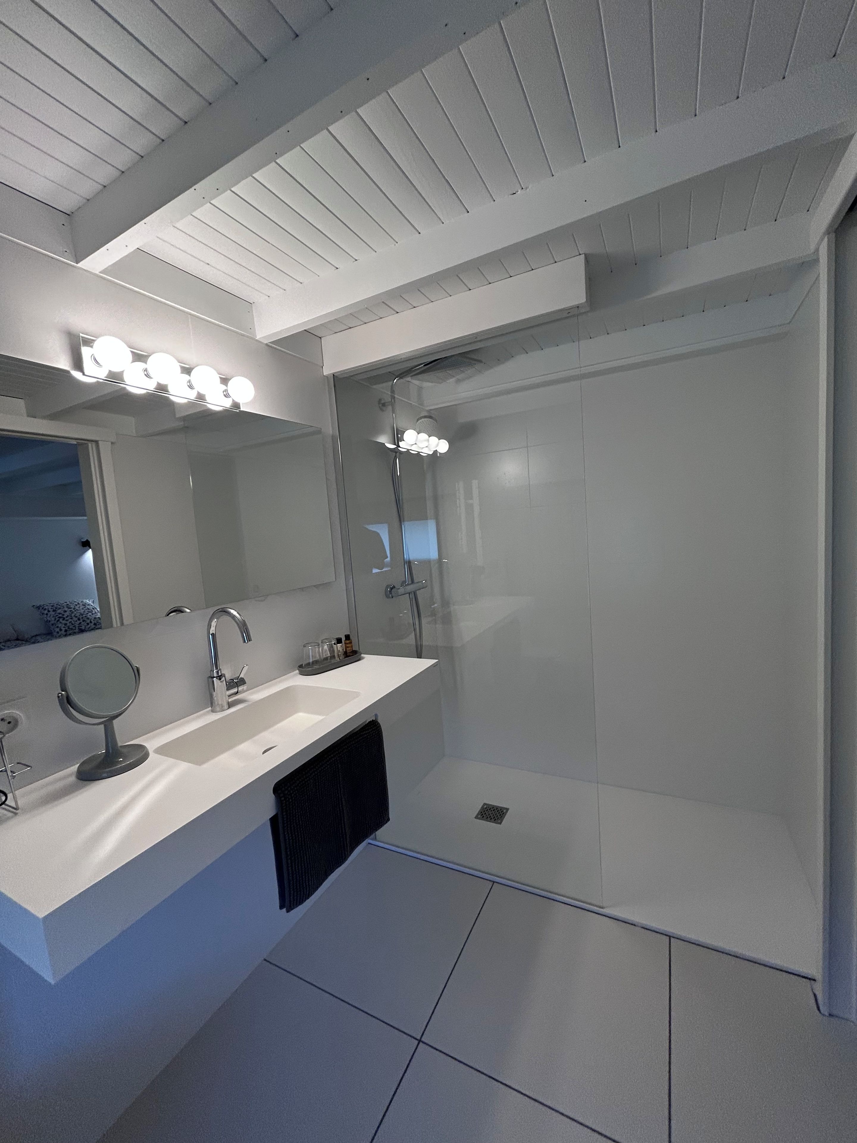Een moderne badkamer met een wit aanrecht, een ronde spiegel, een douche met glazen deur en een plafond met inbouwspots.