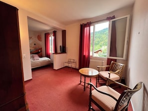 A hotel room with a bed, a desk, a chair, a small table, and a window with a view of greenery. - VICC (Faverges-Seythenex)