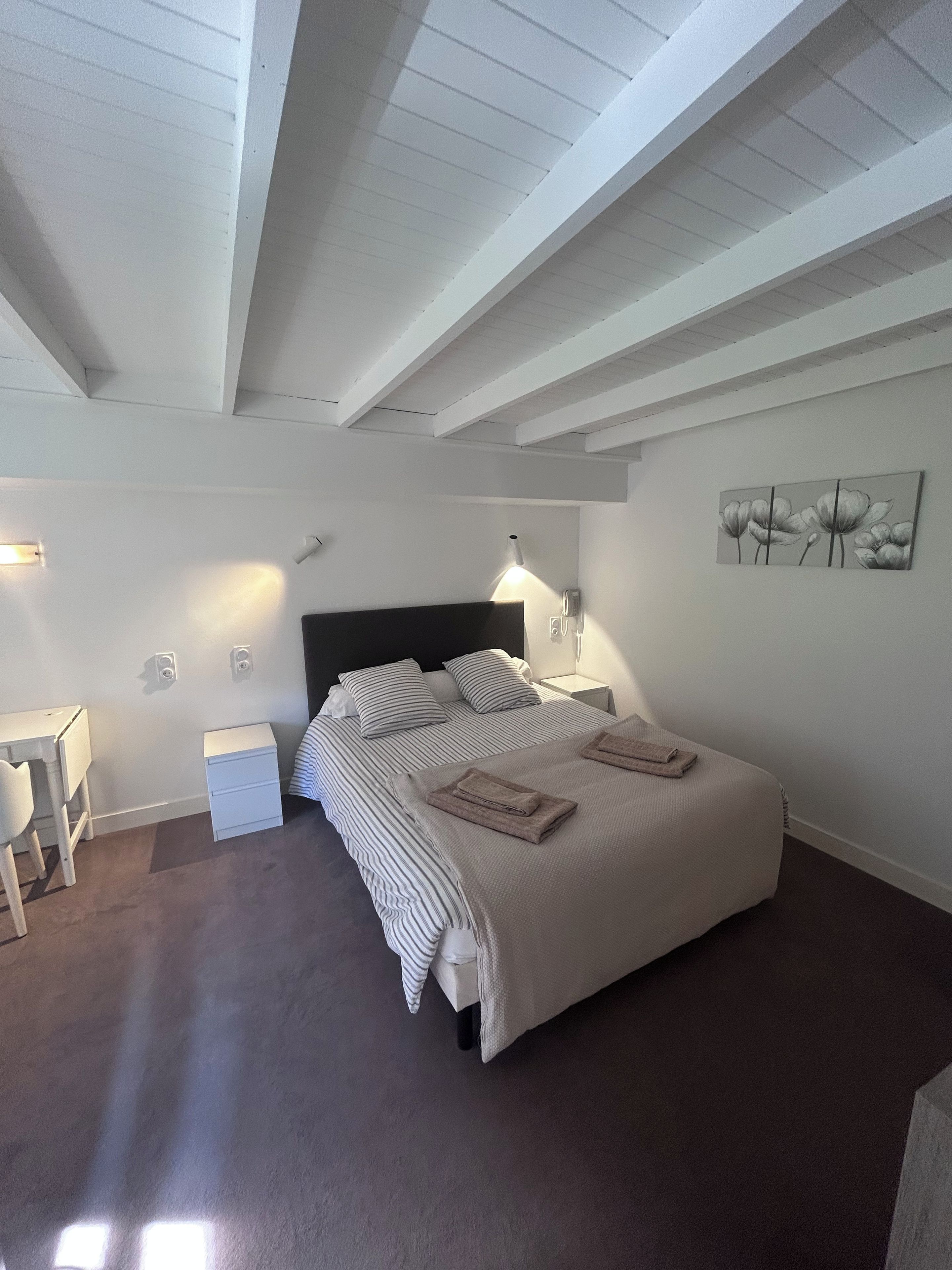 Une chambre à coucher comprenant un lit, des tables de chevet, un bureau et une œuvre d’art accrochée au mur.