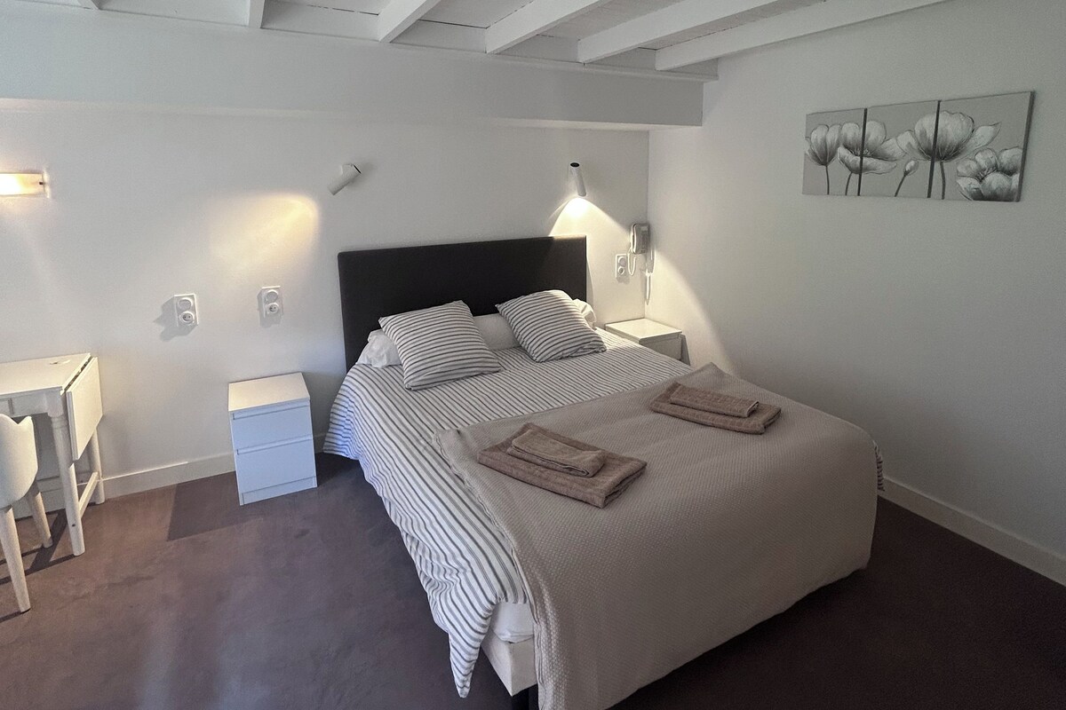 Een slaapkamer met een bed, nachtkastjes, een bureau en een kunstwerk aan de muur.