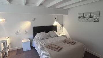 Une chambre à coucher comprenant un lit, des tables de chevet, un bureau et une œuvre d’art accrochée au mur.