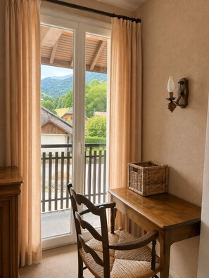 A room with a wooden table, a wicker basket, a chair, and a view of a balcony with a railing. - VICC (Faverges-Seythenex)