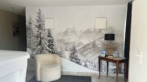 A room with a mountain landscape mural, a white chair, a small table with a lamp, and a door with a handle. - VICC (Faverges-Seythenex)