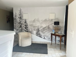 A room with a mountain landscape mural, a white chair, a small table with a lamp, and a door with a handle. - VICC (Faverges-Seythenex)