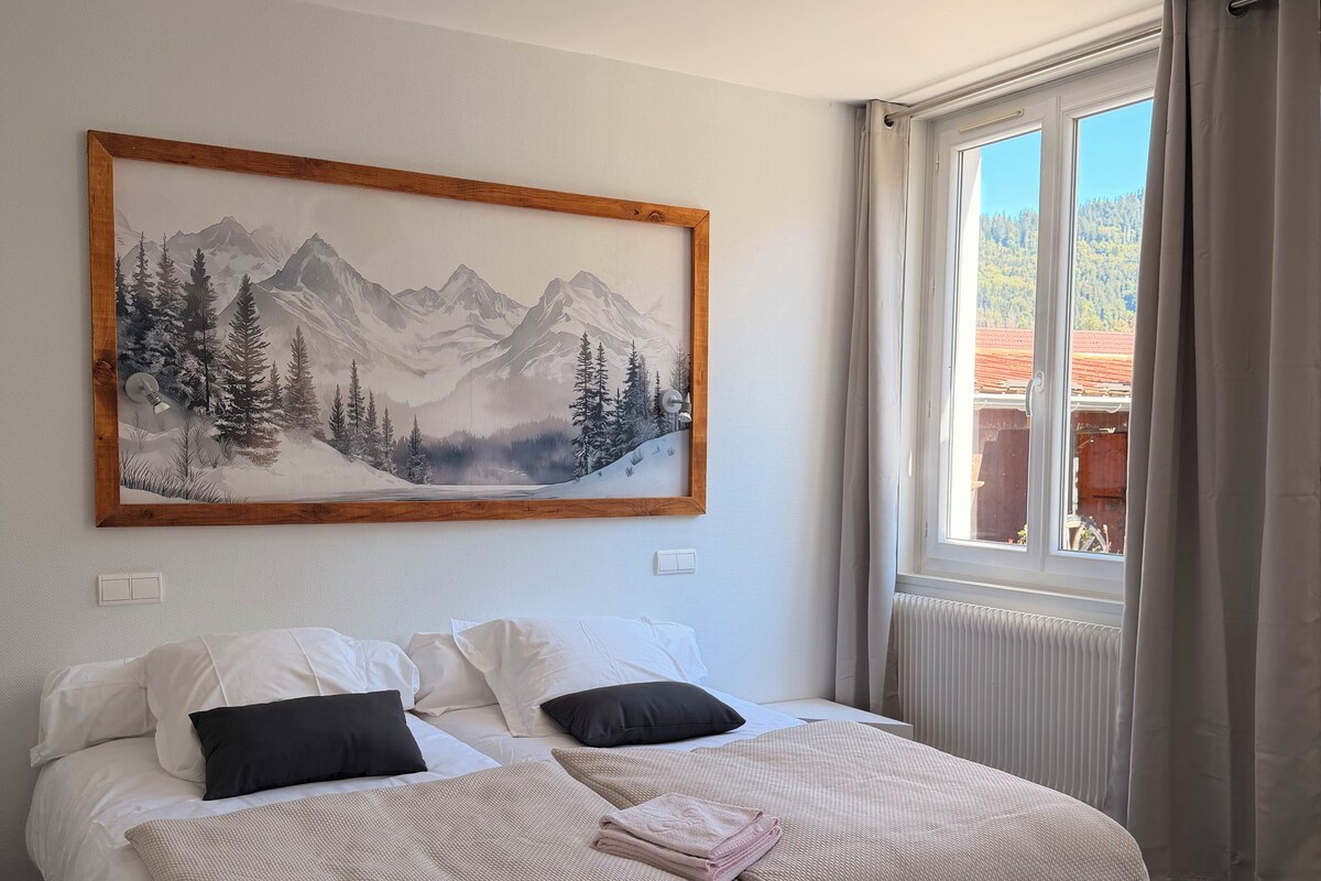 Een hotelkamer met een bed, een schilderij van een berglandschap, een raam met gordijnen en een radiator.