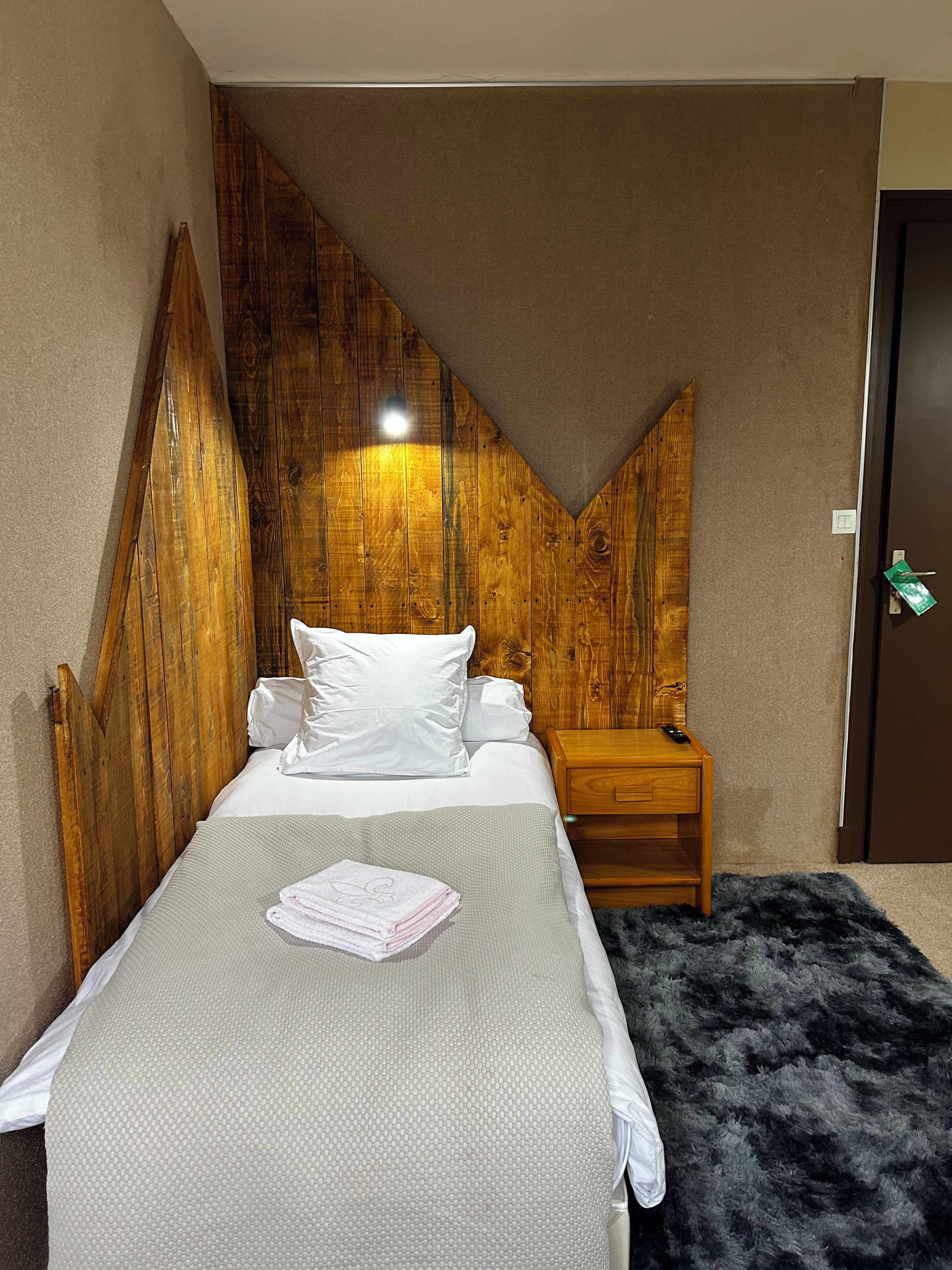 A bedroom with a bed, a nightstand, a remote control, and a door.