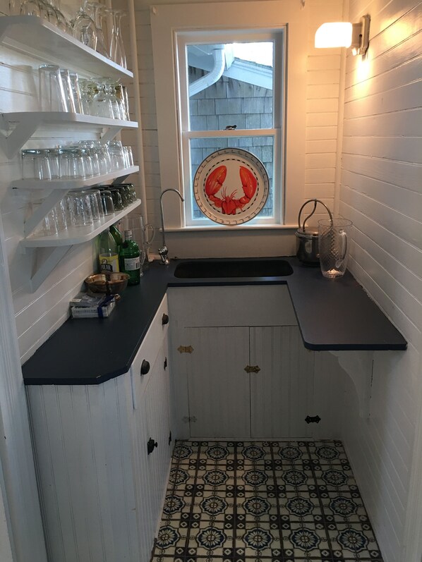 A compact kitchen with white cabinetry, a window with a decorative plate, and a patterned tile floor.