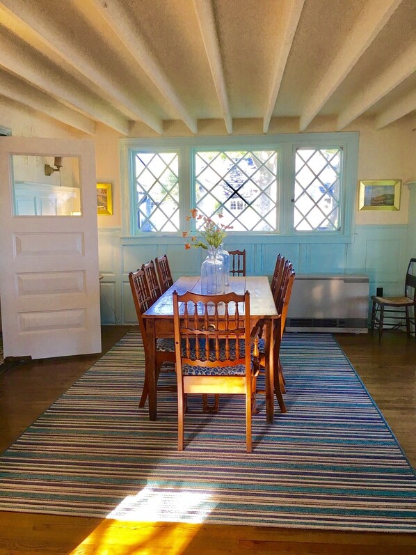 A dining area with a wooden table and chairs, a striped rug, and a view through a window with a lattice design.
