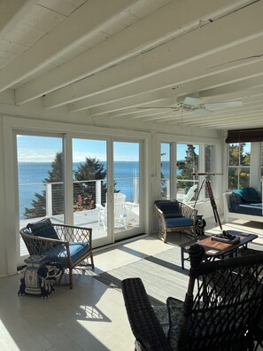 A sunlit room with large windows, wicker furniture, and a view of the sea.