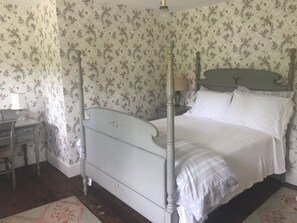 A bedroom with a four-poster bed, a nightstand, a lamp, and floral wallpaper.