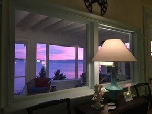 A room with a view of the sea, a window with a lamp, and a chair by the window.