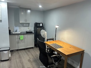 A compact kitchen with a microwave, sink, and a fan. There's a dining table with chairs and a trash bin. - Studio-cozy house Lowertown (Ottawa)