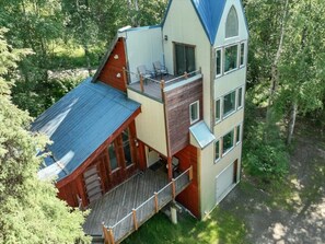 Eine zweistöckige Holzhütte mit einer Veranda, umgeben von Bäumen.