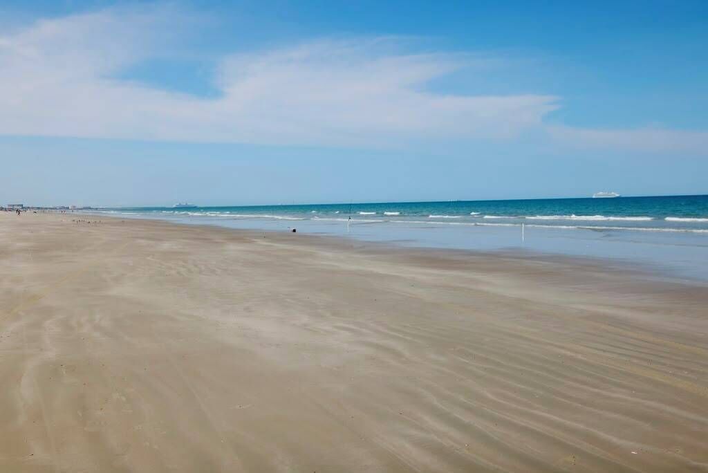 A wide sandy beach with gentle waves and a clear sky.