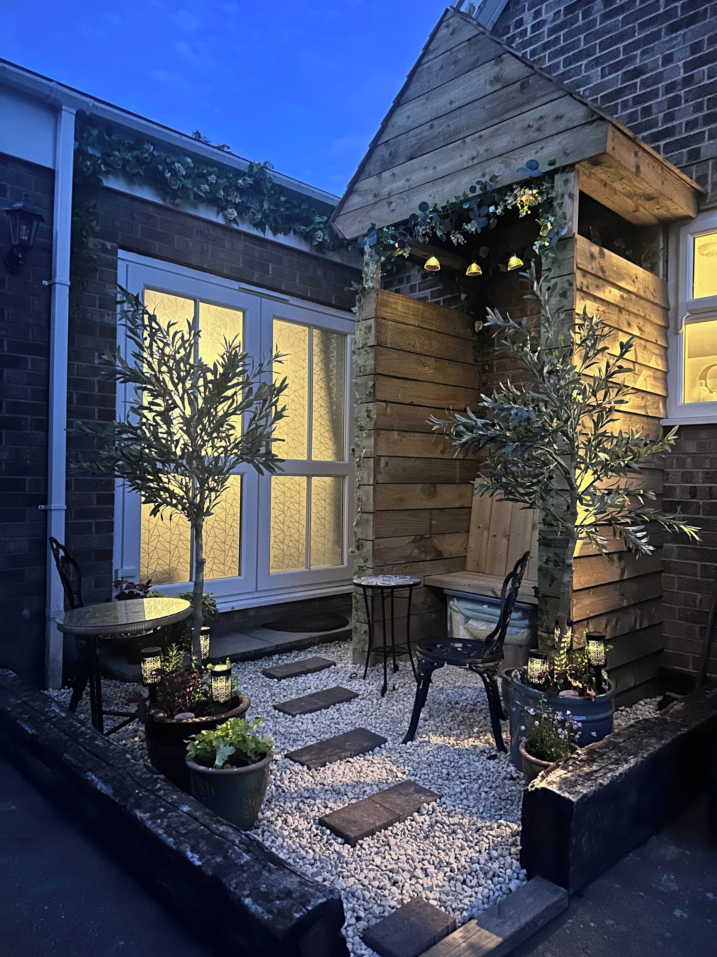A patio area with a wooden pergola, seating, and potted plants.