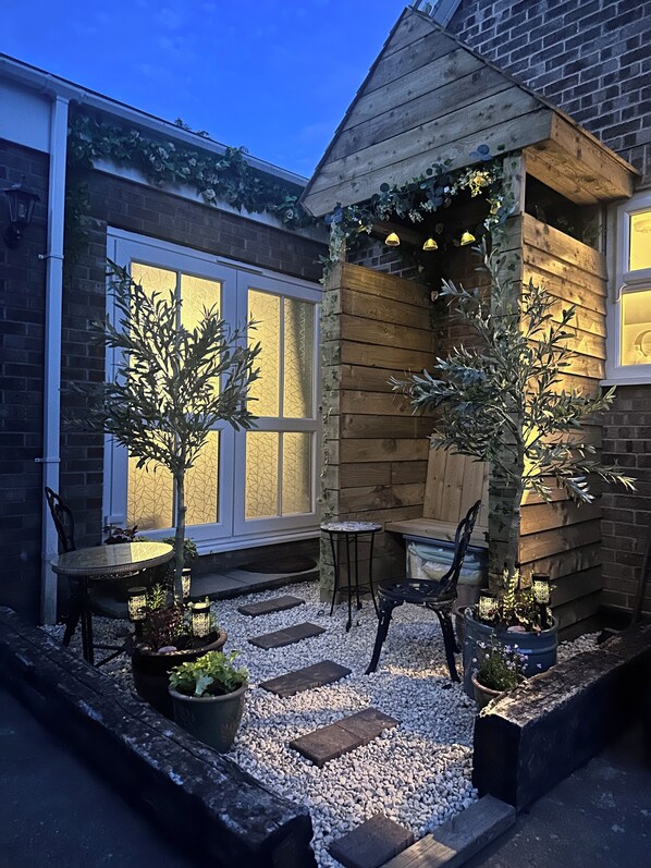 A patio area with a wooden pergola, seating, and potted plants.