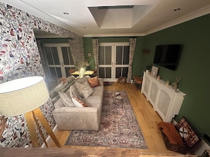 A living room with a sofa, a coffee table, a patterned rug, a cabinet with decorative items, and a television on the wall. - Garden Galley Nook | Coast & Countryside Haven (Sproatley)