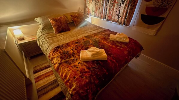 A neatly made bed with a red and orange patterned bedspread, two pillows, and two folded towels on the bed.