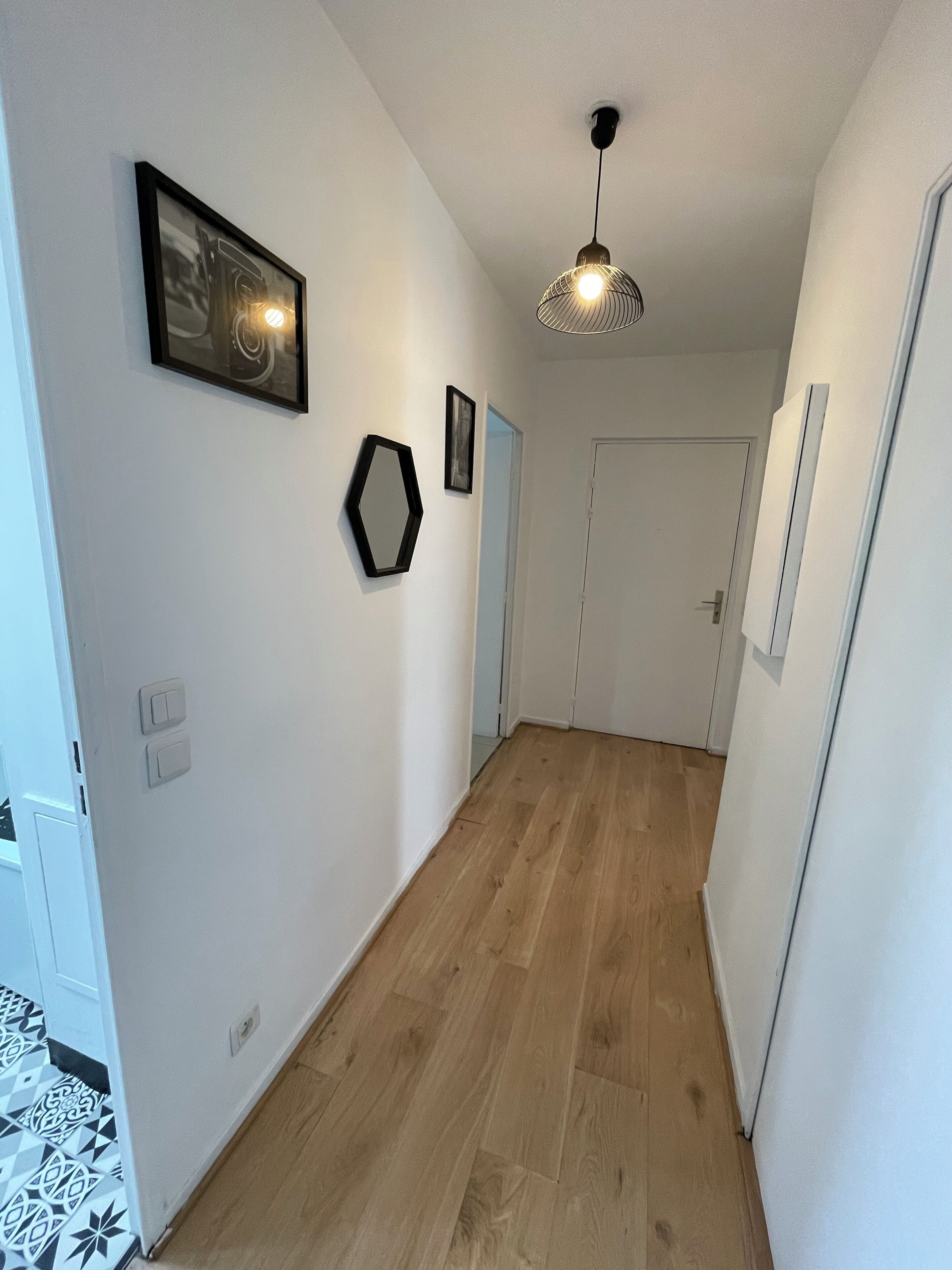 Un couloir doté d’un plancher en bois, de murs blancs et d’un luminaire au plafond.
