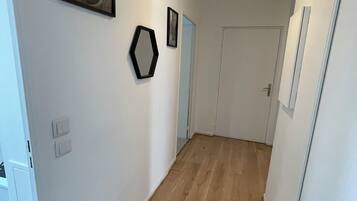 Un couloir doté d’un plancher en bois, de murs blancs et d’un luminaire au plafond.