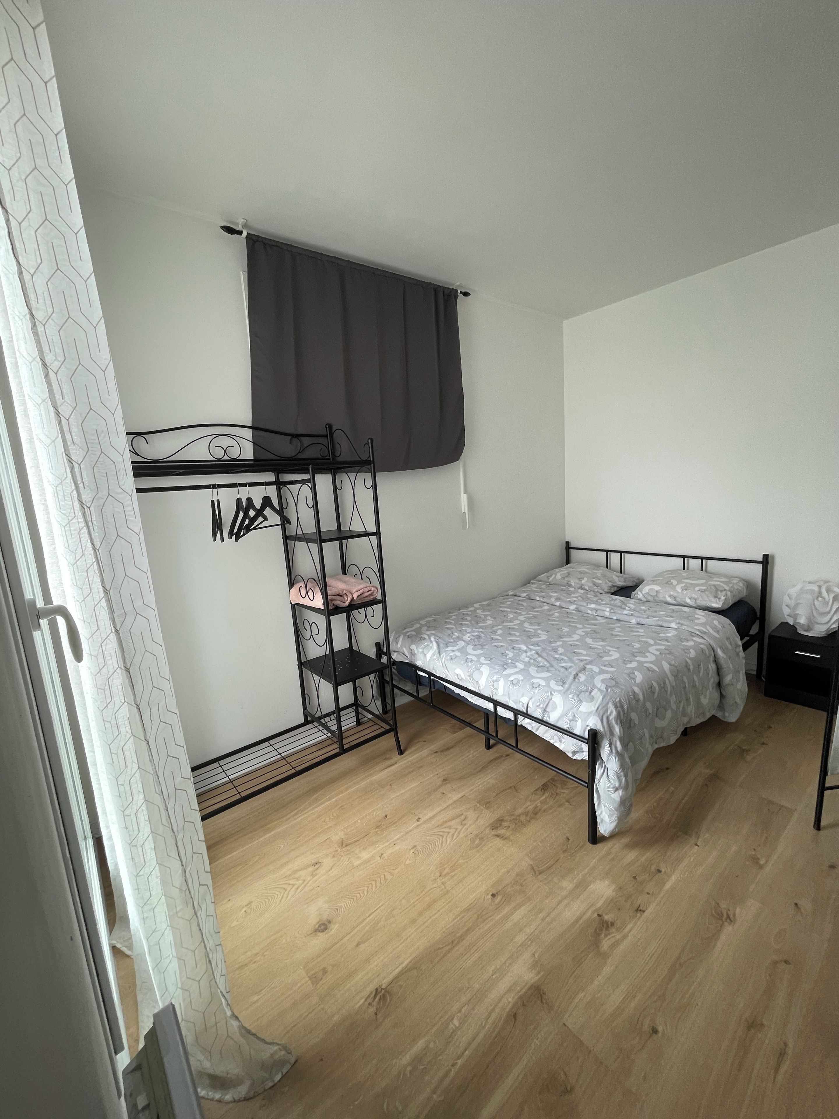 Une chambre à coucher avec un lit, une armoire en métal, une fenêtre avec un rideau et un plancher en bois.