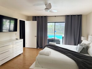 A hotel room with a bed, a TV, a ceiling fan, a sliding door to a balcony, and a view of a swimming pool. - Modern Pool Retreat • Outdoor Kitchen • Fire Pit • Pets (Palm Coast)