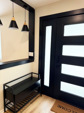 A black door with a window, a black bench, and two pendant lights. - Modern Pool Retreat • Outdoor Kitchen • Fire Pit • Pets (Palm Coast)