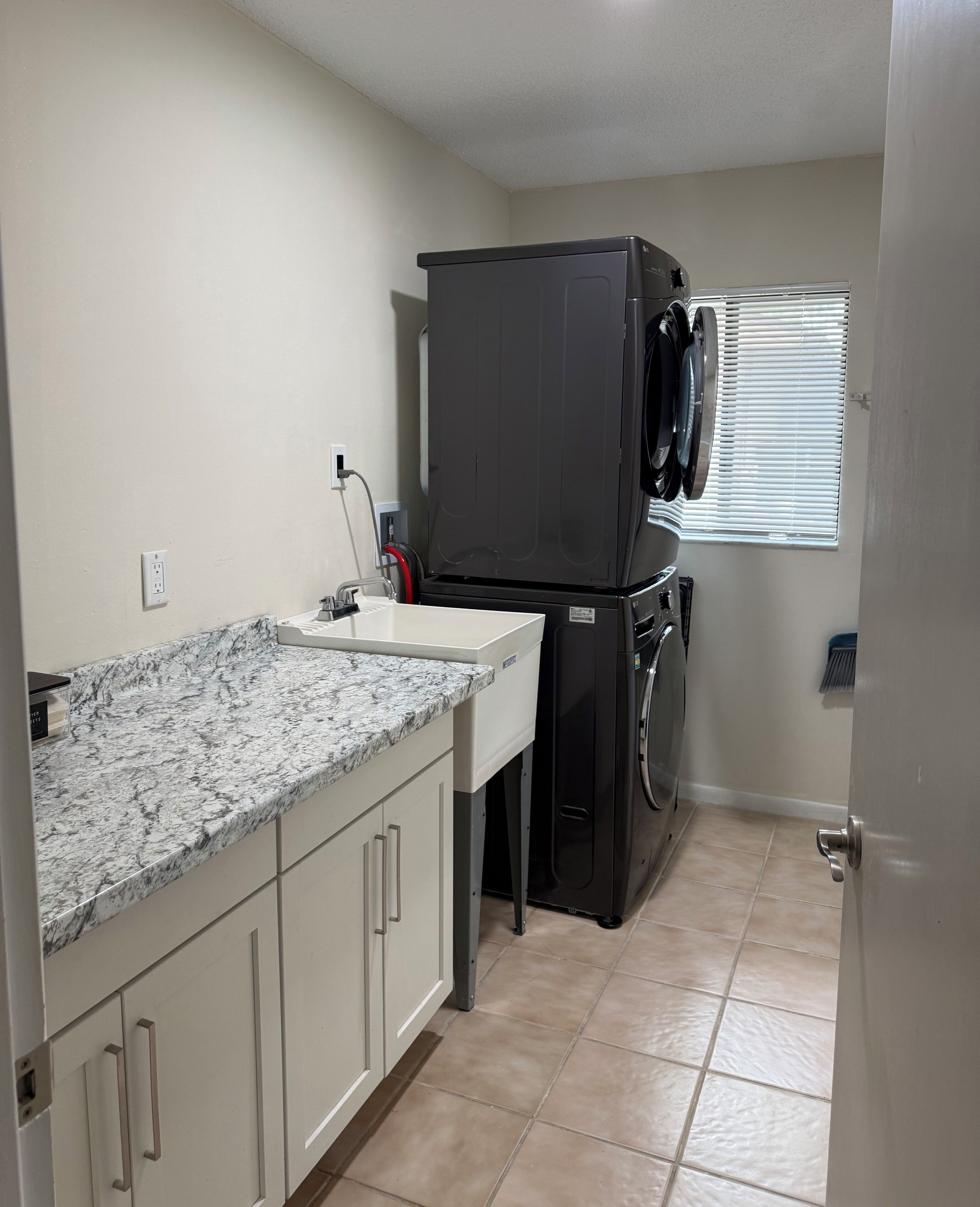A compact kitchen with a built-in washer and dryer, a granite countertop, and a window with blinds.