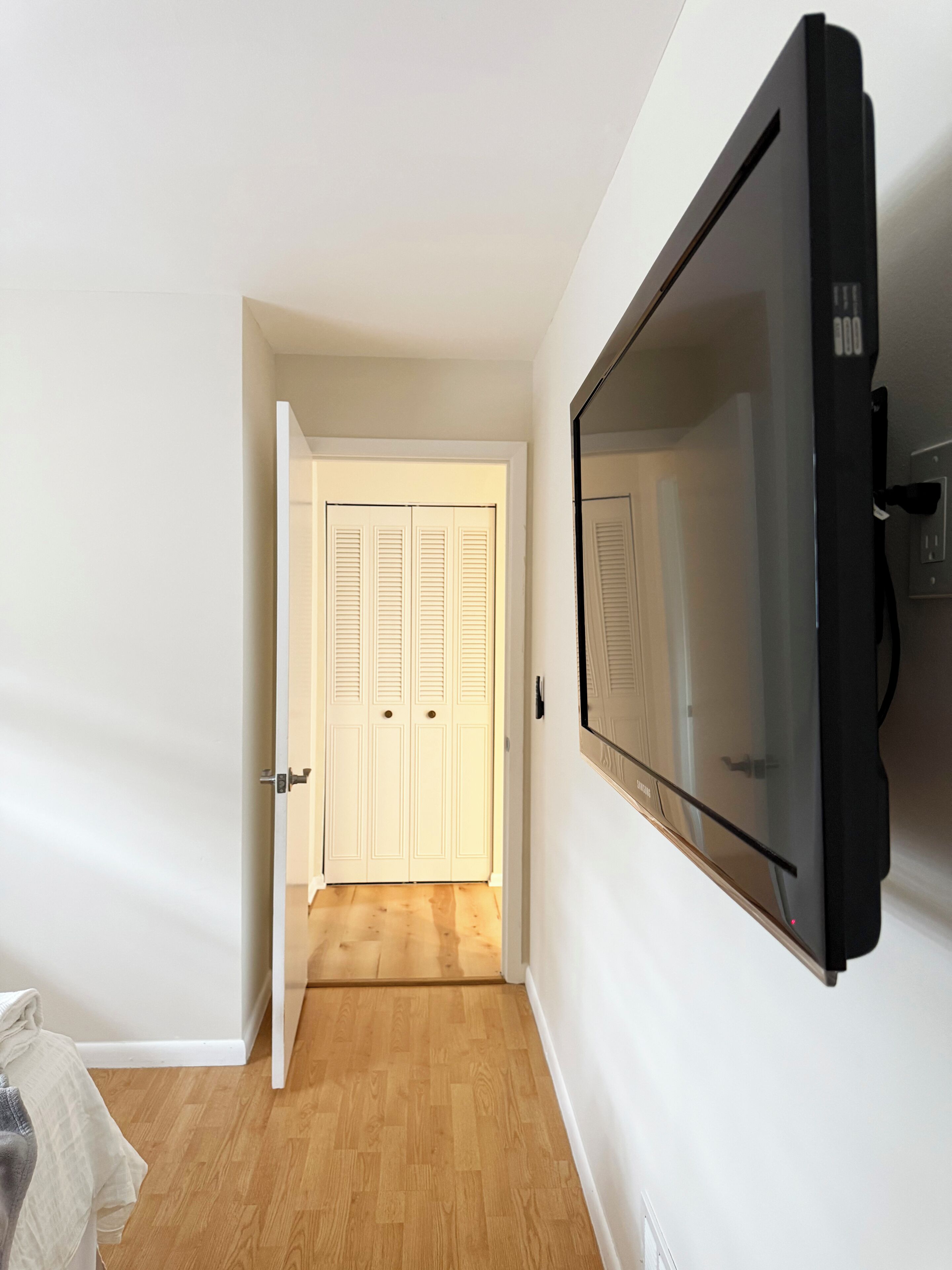 A room with a television mounted on the wall, a door leading to another room, and a wooden floor.