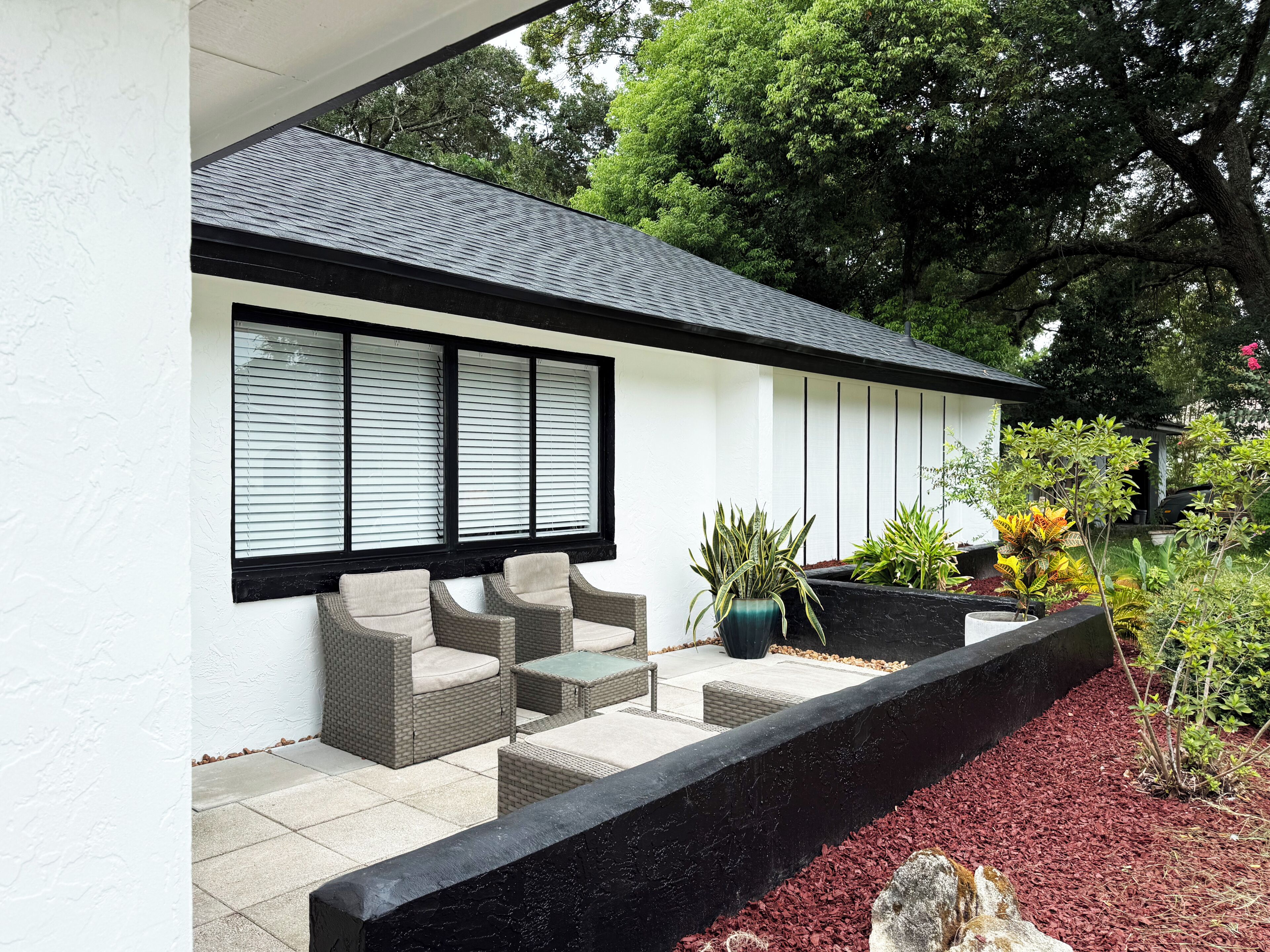 A modern outdoor seating area with wicker furniture and a planter with various plants.