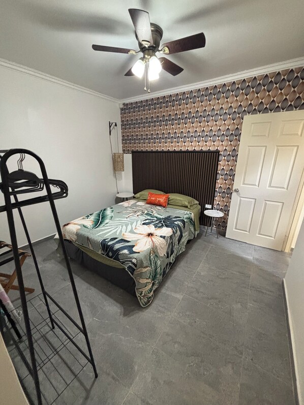 A bedroom with a bed, a ceiling fan, a wall with a geometric pattern, and a door.
