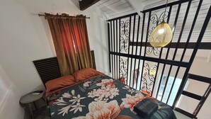 A bedroom with a bed, curtains, a small table, and a decorative wall panel. - Authentic Rincon, a touch of vintage charm (Rincon)