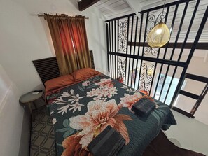 Ein Schlafzimmer mit Bett, Vorhängen, einem kleinen Tisch und einer dekorativen Wandverkleidung.