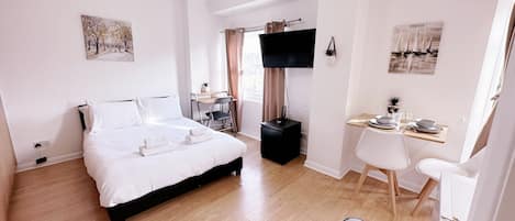 A hotel room with a bed, a desk, a chair, a TV, and artwork on the walls.