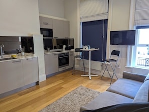 Eine moderne Küche mit Mikrowelle, Backofen und Spüle. Ein Essbereich mit Tisch und Stühlen ist vorhanden. Ein Flachbildfernseher ist an der Wand befestigt.