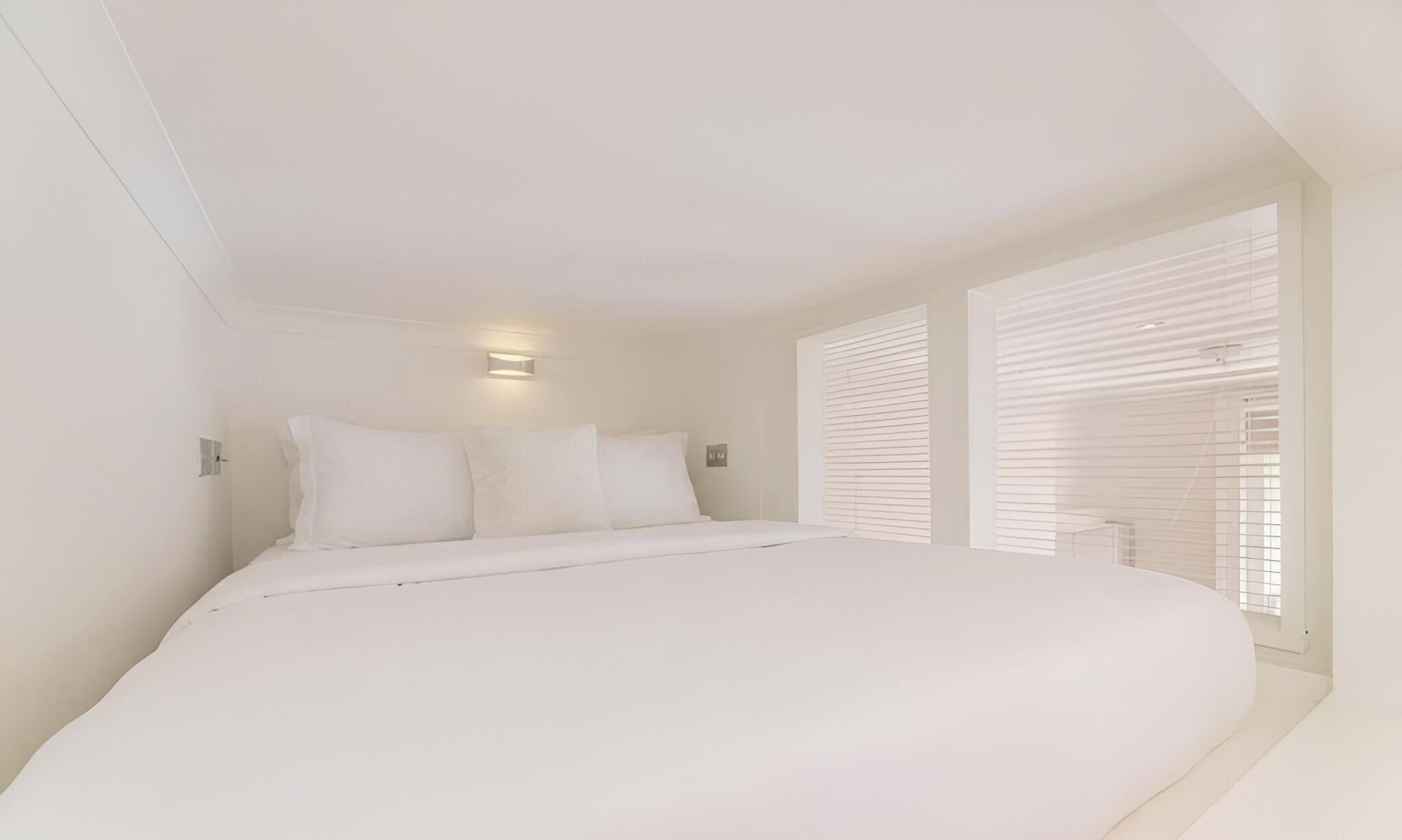Een slaapkamer met een groot bed, twee bedlampjes en een raam met zonwering.