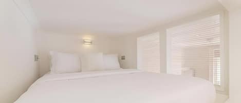 A bedroom with a large bed, two bedside lamps, and a window with blinds.