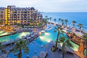 A resort with multiple swimming pools, palm trees, and a view of the ocean. - Villa Del Arco 1 bedroom Suite in Cabo San Lucas during Bisbee Week (Cabo San Lucas)