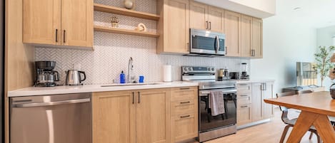 A modern kitchen with wooden cabinets, stainless steel appliances, and a dining area with a wooden table.