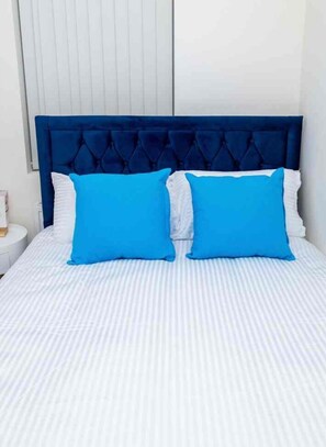 A bed with a tufted headboard and two bright blue pillows. - Cozy and Beautiful 3-Bed House in Manchester!
Sleeps 6 Comfortably! (Salford)